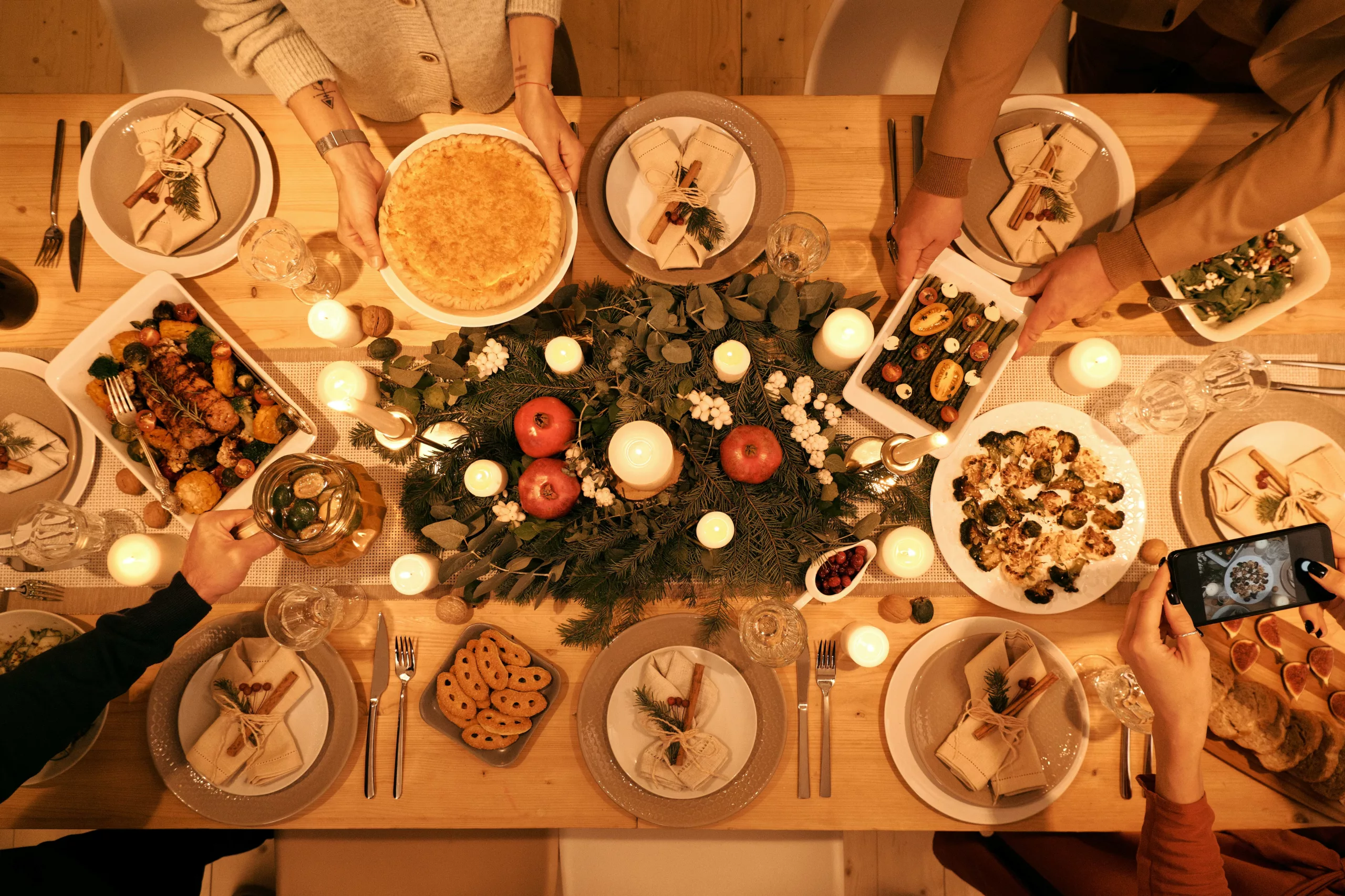 A beautifully decorated holiday dinner table with festive food, decor, and people capturing memories.